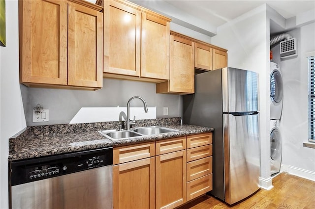 kitchen featuring visible vents, light wood finished floors, a sink, stainless steel appliances, and stacked washer and clothes dryer