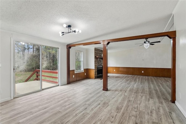 unfurnished living room with ceiling fan with notable chandelier, a textured ceiling, wood finished floors, a large fireplace, and wainscoting