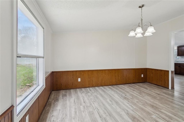 empty room with wooden walls, light wood-style flooring, wainscoting, a textured ceiling, and a chandelier