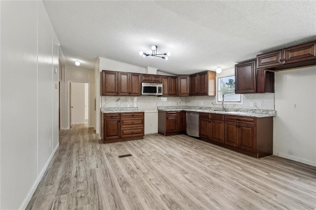 kitchen with backsplash, vaulted ceiling, light wood-style floors, stainless steel appliances, and a sink