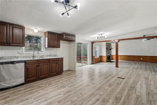 kitchen featuring light stone countertops, stainless steel dishwasher, light wood-style floors, a textured ceiling, and a sink