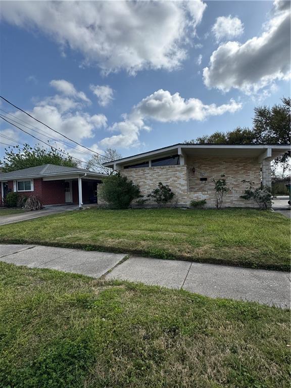 view of side of property featuring stone siding, a carport, driveway, and a lawn