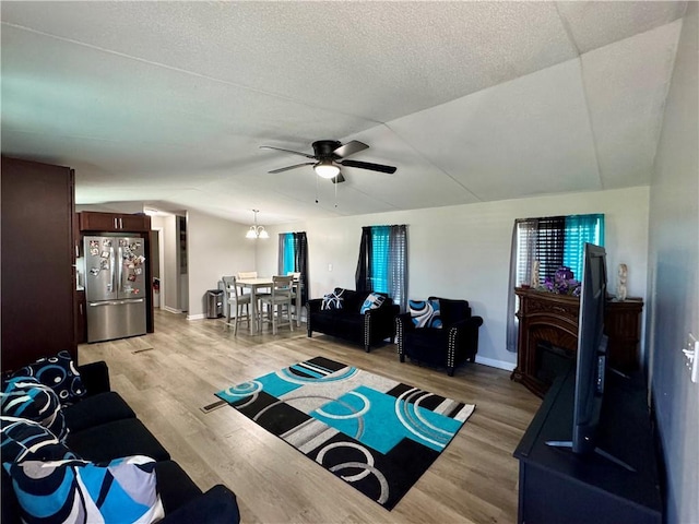 living area featuring light wood-type flooring, a ceiling fan, a textured ceiling, a fireplace, and lofted ceiling