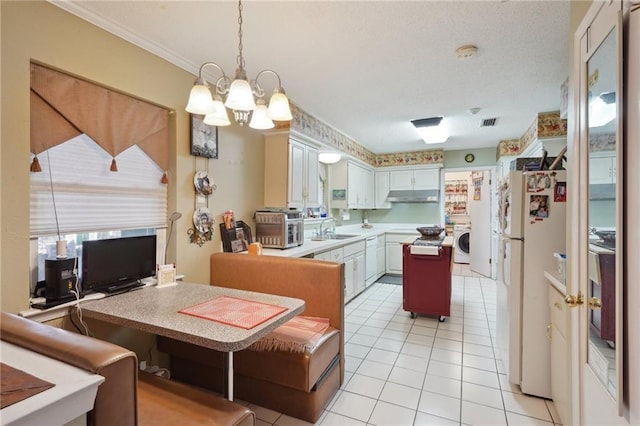 kitchen with under cabinet range hood, a chandelier, freestanding refrigerator, washer / clothes dryer, and a sink