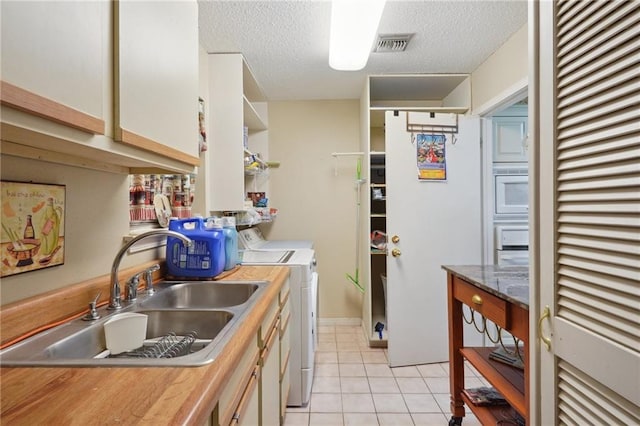 kitchen with visible vents, a sink, a textured ceiling, separate washer and dryer, and light tile patterned flooring