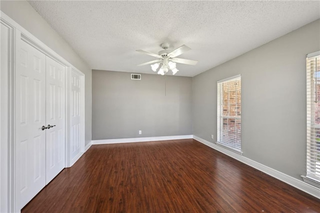 unfurnished bedroom with a ceiling fan, baseboards, visible vents, dark wood finished floors, and a closet