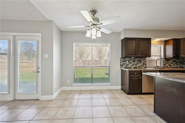 kitchen with dark brown cabinetry, light tile patterned floors, backsplash, and stainless steel dishwasher