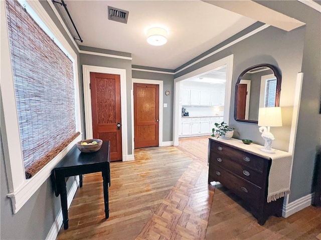 hall with parquet floors, baseboards, visible vents, and ornamental molding