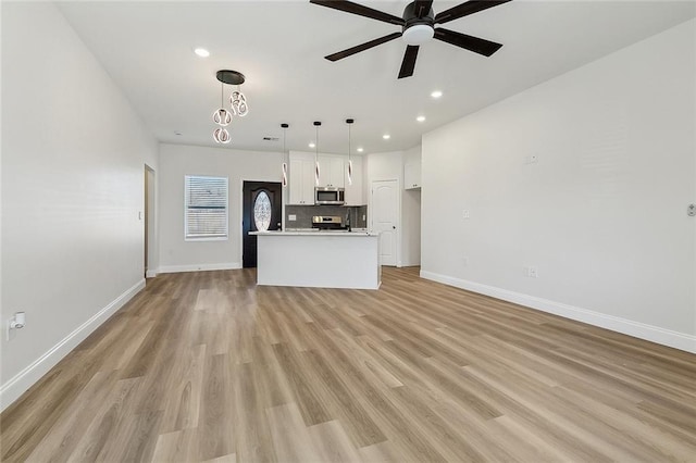 kitchen with light wood finished floors, white cabinets, ceiling fan with notable chandelier, open floor plan, and backsplash