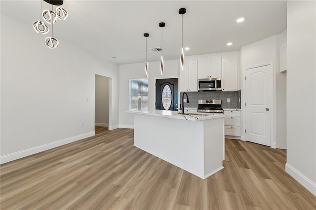 kitchen featuring light wood finished floors, decorative backsplash, white cabinets, stainless steel appliances, and a sink