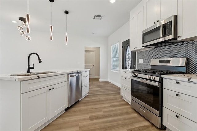 kitchen with backsplash, appliances with stainless steel finishes, light wood-style floors, white cabinets, and a sink