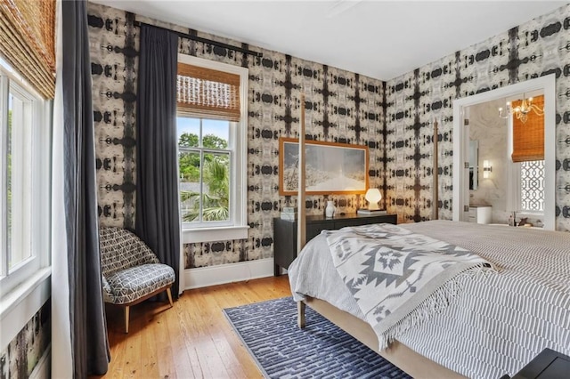 bedroom featuring baseboards, a notable chandelier, hardwood / wood-style floors, and wallpapered walls