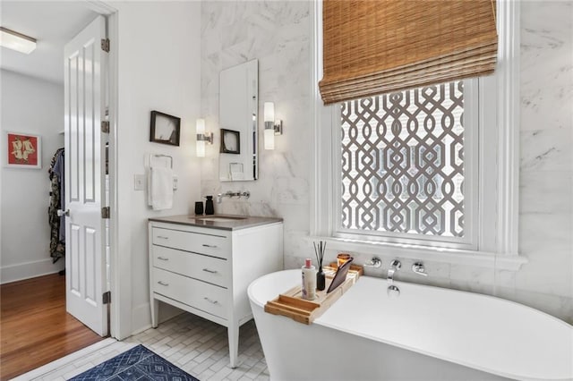 bathroom with a freestanding bath, vanity, tile walls, and wood finished floors