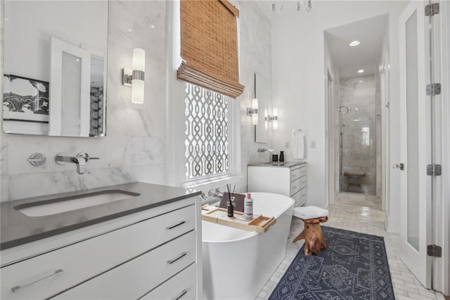 full bathroom with a shower stall, two vanities, a freestanding tub, tile walls, and a sink