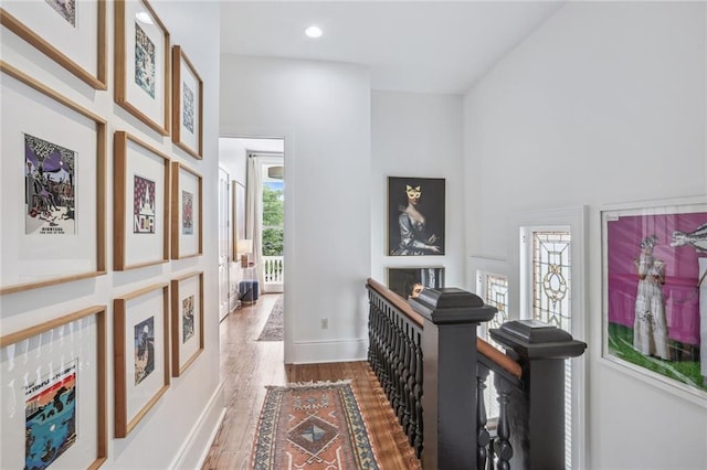 hallway featuring recessed lighting, baseboards, wood finished floors, and a towering ceiling