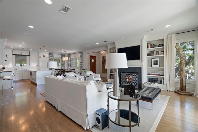 living area with recessed lighting, visible vents, a lit fireplace, and light wood-type flooring