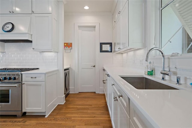 kitchen featuring high end range, washer / clothes dryer, a sink, custom range hood, and white cabinets