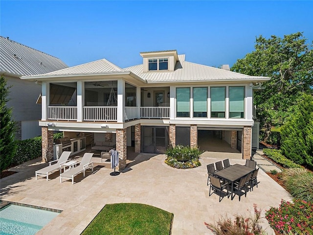 back of property featuring stone siding, metal roof, a patio, and a sunroom