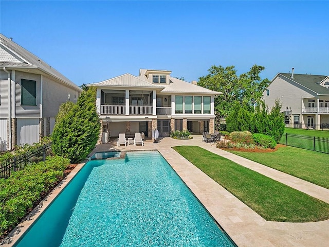 rear view of house with a lawn, a pool with connected hot tub, fence, a balcony, and a patio area