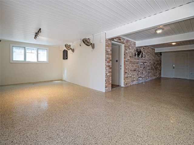 unfurnished room featuring beam ceiling, brick wall, and speckled floor