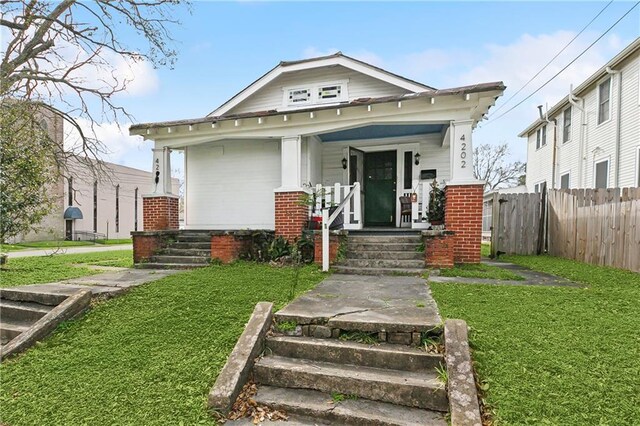 view of front of home with a front yard, covered porch, fence, and brick siding