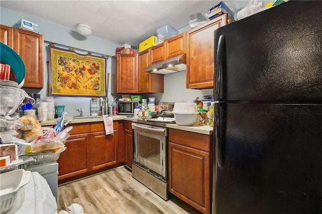 kitchen featuring light countertops, freestanding refrigerator, stainless steel range with electric stovetop, light wood-type flooring, and under cabinet range hood