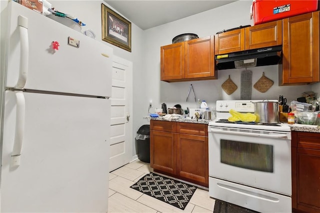 kitchen featuring brown cabinets, light countertops, under cabinet range hood, and white appliances