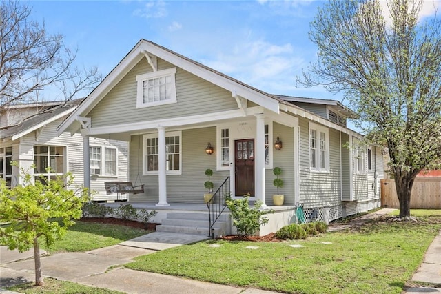 bungalow-style home with covered porch, a front lawn, and fence