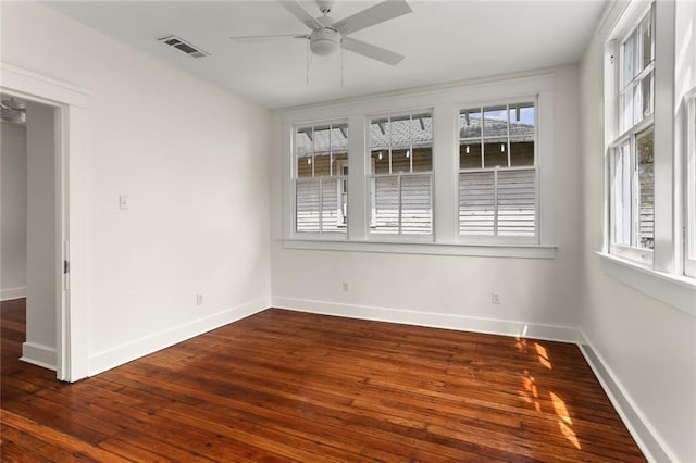 empty room with dark wood-style floors, visible vents, baseboards, and a ceiling fan