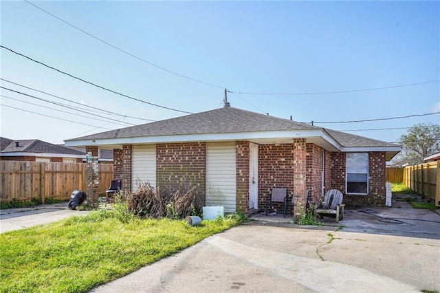 view of side of home with a patio area, brick siding, roof with shingles, and fence