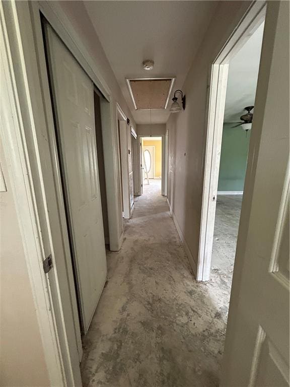 corridor with attic access, concrete floors, and baseboards