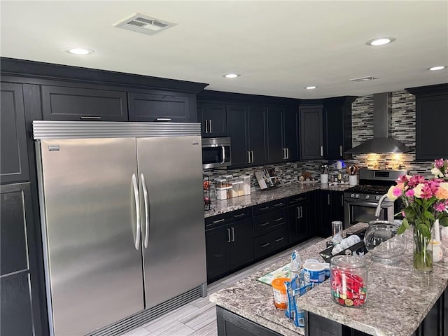 kitchen featuring tasteful backsplash, visible vents, wall chimney range hood, stainless steel appliances, and dark cabinets