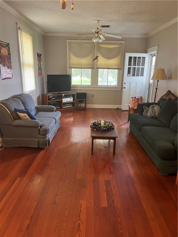 living room featuring visible vents, a textured ceiling, crown molding, and wood finished floors