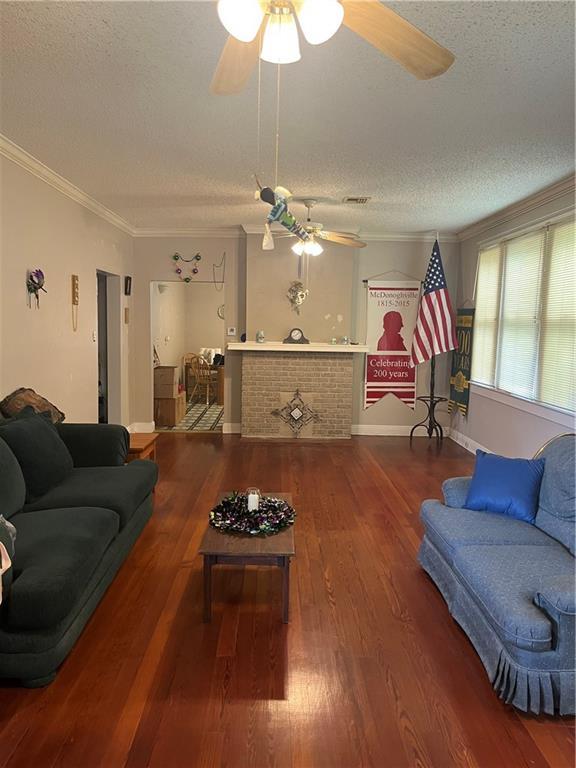 living room featuring wood finished floors, a textured ceiling, ornamental molding, and a ceiling fan