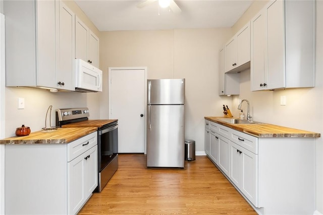 kitchen with light wood-style flooring, a sink, ceiling fan, appliances with stainless steel finishes, and butcher block counters