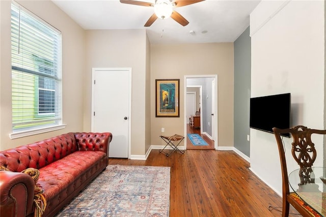 living area featuring baseboards, a ceiling fan, and hardwood / wood-style flooring