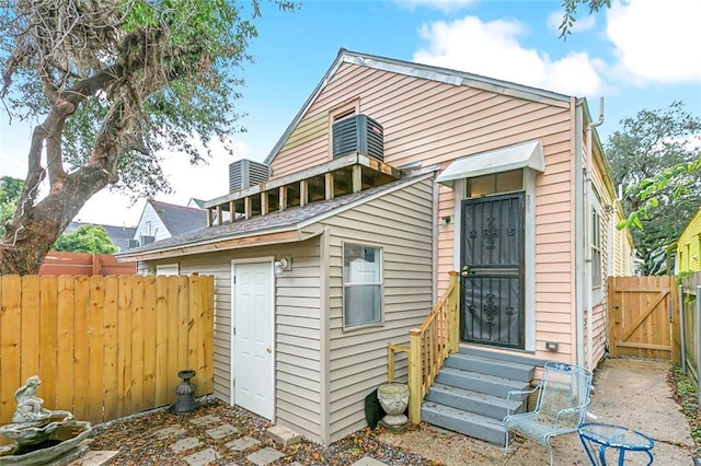 rear view of house featuring a gate, entry steps, central AC unit, and fence