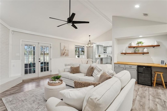 living room featuring lofted ceiling, beverage cooler, wainscoting, and ceiling fan with notable chandelier