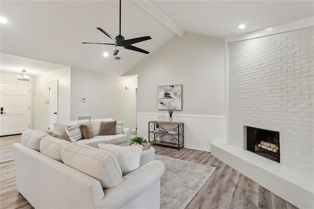 living area featuring wood finished floors, visible vents, a fireplace, ceiling fan, and beamed ceiling