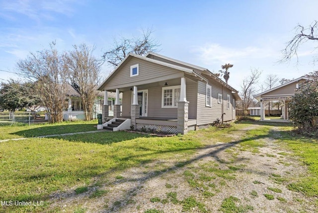 view of front facade with covered porch, driveway, a front yard, and fence