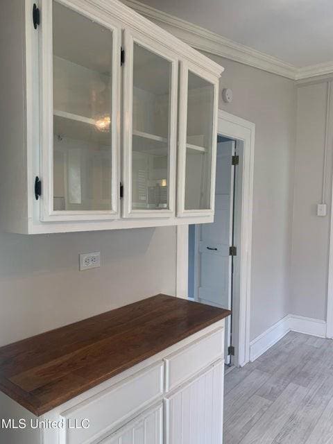 kitchen featuring ornamental molding, light wood-style flooring, white cabinetry, glass insert cabinets, and baseboards