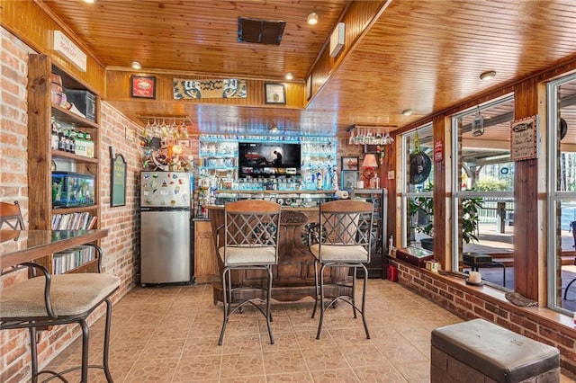 interior space featuring wooden ceiling, brick wall, and freestanding refrigerator