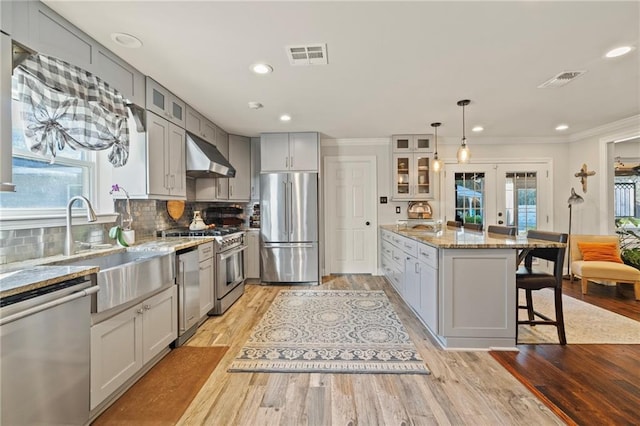 kitchen featuring high end appliances, visible vents, glass insert cabinets, under cabinet range hood, and a kitchen bar