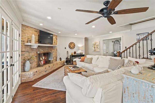 living room with wood finished floors, ceiling fan, stairs, crown molding, and a brick fireplace