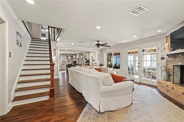 living area with stairway, a ceiling fan, visible vents, a fireplace, and hardwood / wood-style flooring