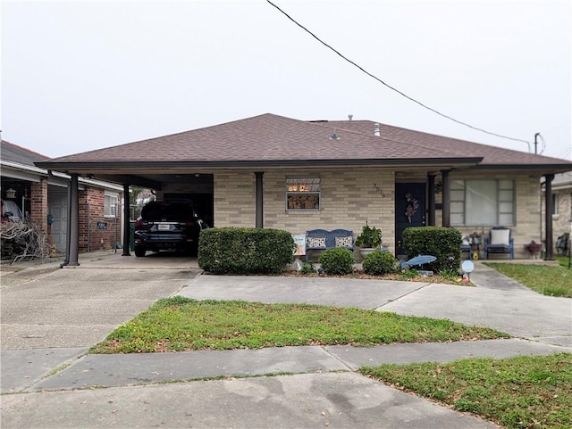 view of front of house featuring concrete driveway, an attached carport, roof with shingles, and brick siding
