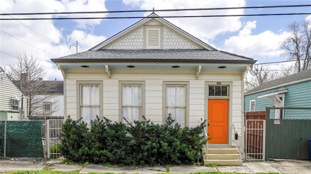 shotgun-style home with entry steps, fence, and a shingled roof