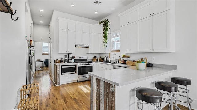 kitchen with visible vents, a peninsula, a sink, stainless steel appliances, and under cabinet range hood