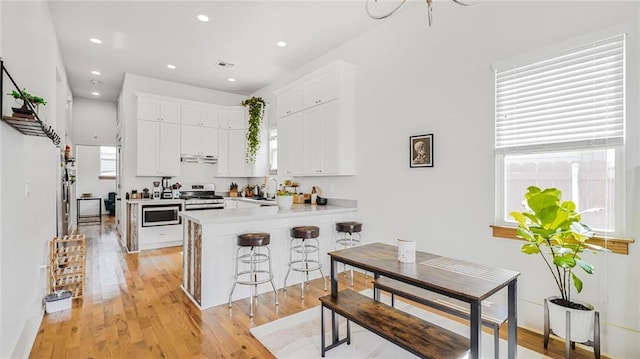 kitchen featuring a peninsula, light wood-style flooring, under cabinet range hood, white cabinetry, and stainless steel gas stove