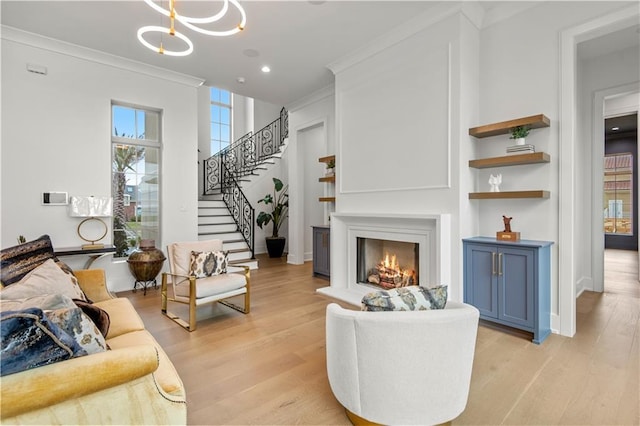 living area featuring light wood-type flooring, ornamental molding, a lit fireplace, baseboards, and stairs